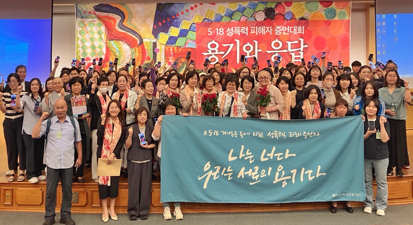 2024년 9월 30일 국회에서 열린 5&middot;18 성폭력 피해자 증언대회 「용기와 응답」 참석자들의 단체 사진이다. 참석자들이 휴대전화를 들어 올리거나 주먹을 쥐고 무대 위에 모여 있고, 앞쪽에 &ldquo;#5&middot;18 계엄군 등에 의한 성폭력 피해 증언자 나는 너다 우리는 서로의 용기다&rdquo;라고 적힌 현수막을 펼쳐 들고 있다. 가운데 몇몇 참석자는 붉은 장미 꽃다발을 들고 있다.