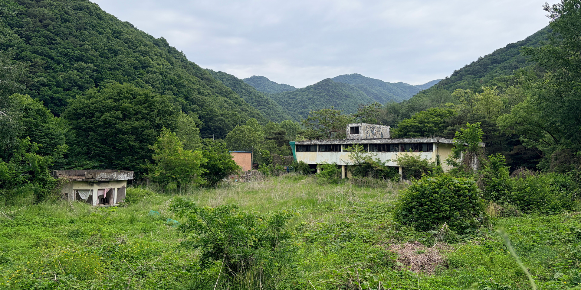 동두천-의정부 기지촌 답사에서 찾은 옛 성병관리소 모습이다. 산자락 아래 무성한 풀과 나무에 둘러싸인 낡은 2층 건물이 있고, 사진 왼쪽에 작은 경비시설 건물이 보인다.