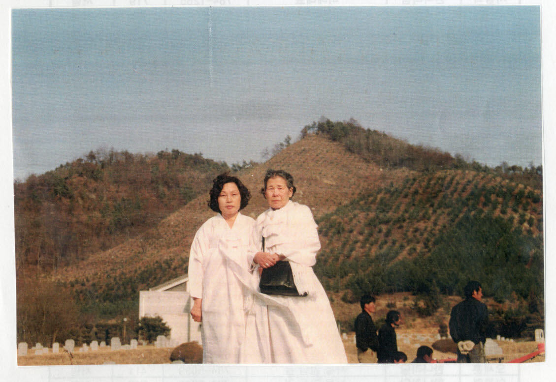 1993년 망향의 동산에서 김학순 할머니와 이희자 씨가 나란히 서서 찍은 사진이다. 두 사람 모두 흰 한복 차림이며, 뒤로 묘비가 늘어선 묘역과 나무가 심긴 산이 보인다.