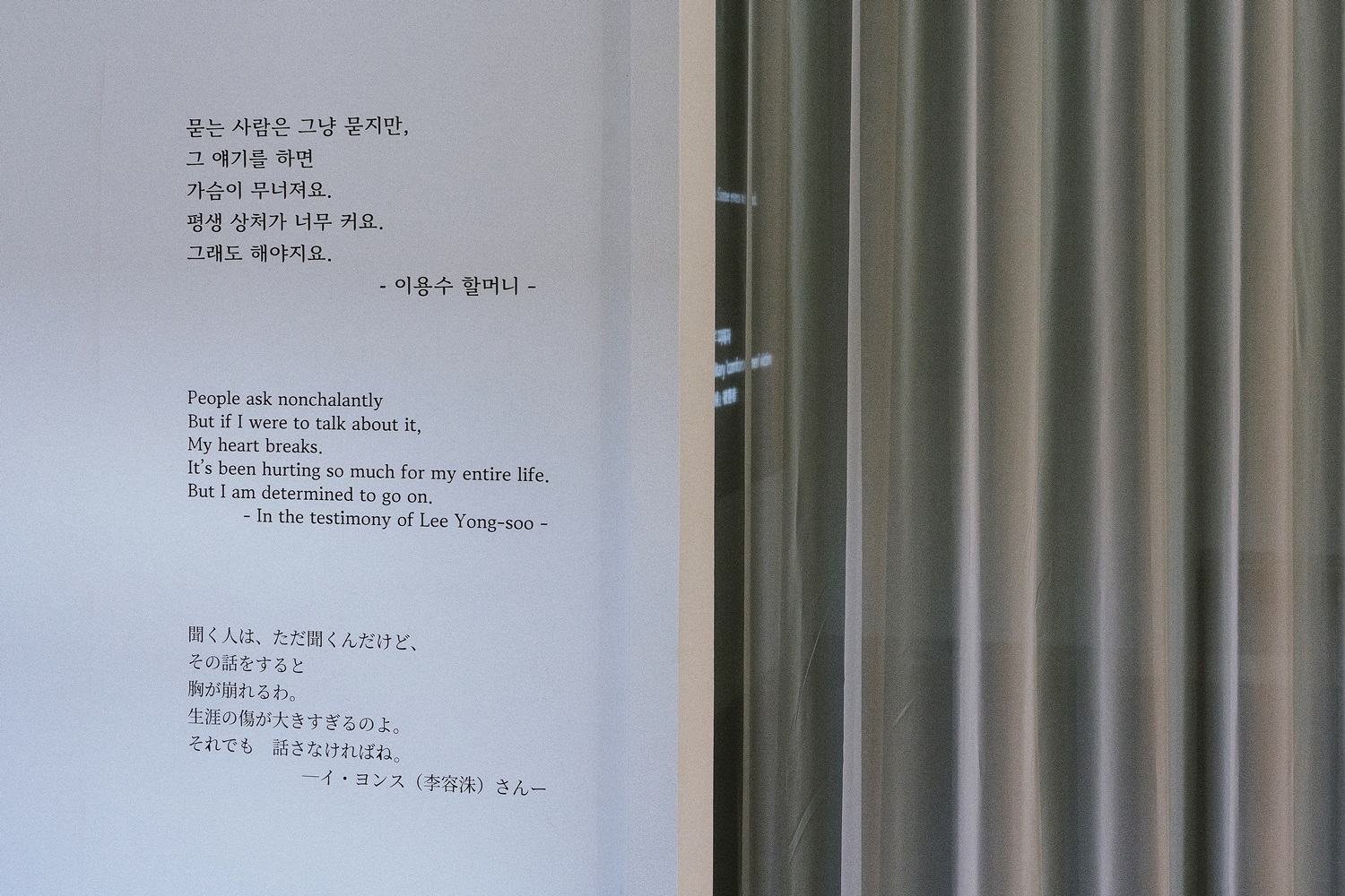 이용수 할머니의 증언 &ldquo;묻는 사람은 그냥 묻지만, 그 얘기를 하면 가슴이 무너져요. 평생 상처가 너무 커요. 그래도 해야지요.&rdquo;가 한국어, 영어, 일본어로 적힌 벽과 회색 커튼이다.