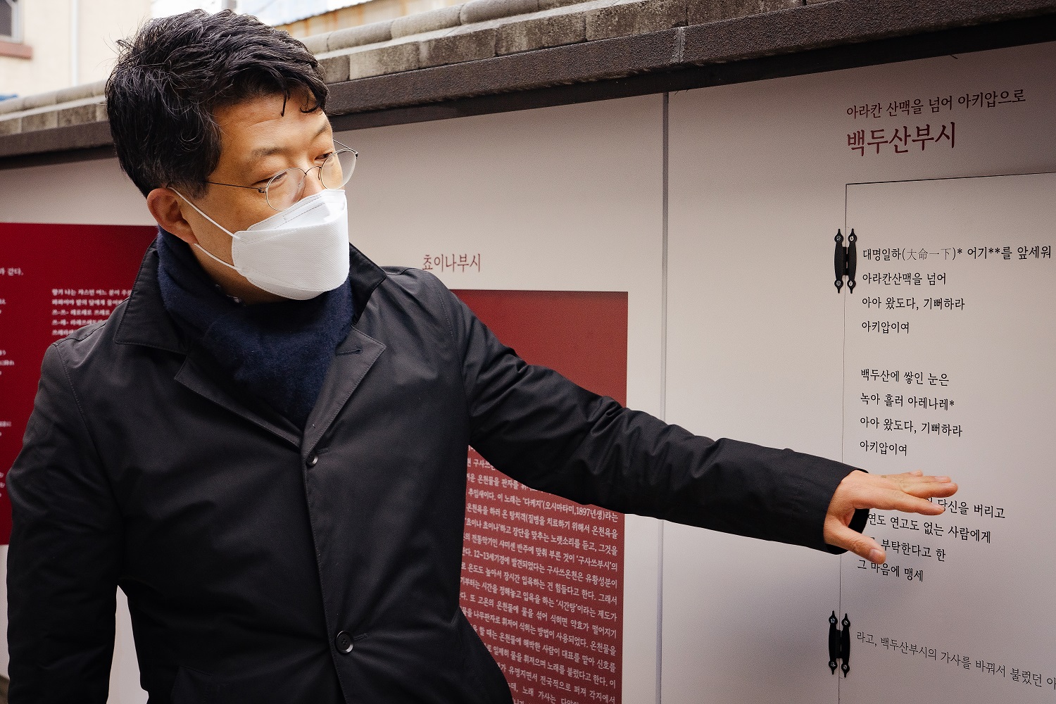 서혁수 대표가 야외 전시 벽의 &lsquo;백두산부시&rsquo; 노래 가사 패널을 손으로 가리키며 설명하고 있다.