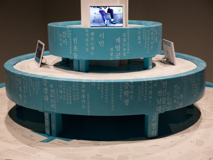 하늘색 원형 단을 2단으로 쌓은 설치 작품이다. 단의 둘레에 &lsquo;시민&rsquo;, &lsquo;계엄군&rsquo;, &lsquo;중학생&rsquo; 등의 낱말이 적혀 있고, 위에 영상 화면들이 놓여 있다.